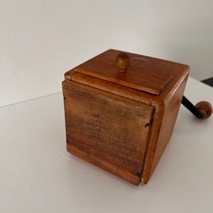 Puede incluir: Un molinillo de caf&eacute; cuadrado de madera con acabado marr&oacute;n medio, que presenta una tapa superior con bisagras y un peque&ntilde;o pomo redondo de madera, un caj&oacute;n frontal con veta de madera oscura y una manivela de metal negro con un pomo de madera.