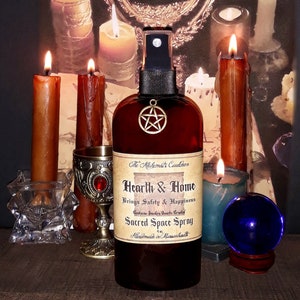 May include: A brown bottle of "Hearth & Home Sacred Space Spray" with a pentagram charm, surrounded by lit candles, a chalice, and a blue crystal ball. The text on the bottle reads "Brings Safety & Happiness". The background includes a mirror.