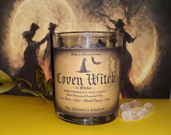 May include: A clear glass jar candle with a tan label featuring the text Coven Witch, 13 Witches, Hand Poured Soy Wax Candle, With Botanical Essential Oils, Star Anise, Clove, Black Pepper, Sage, and The Alchemist's Cauldron with a witch hat icon.