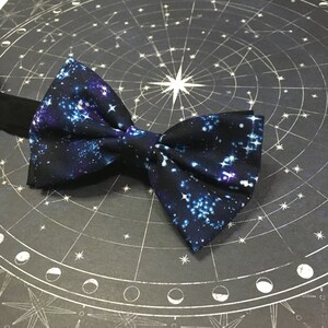 May include: A navy blue bow tie with a white galaxy print. The bow tie is made of a soft, comfortable fabric and is perfect for adding a touch of style to any outfit.