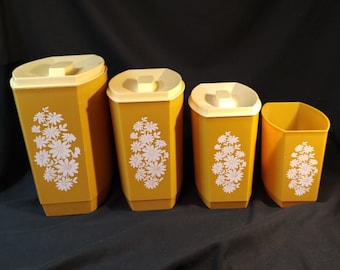 May include: Set of four yellow canisters with white floral designs. The canisters are different sizes and have lids.