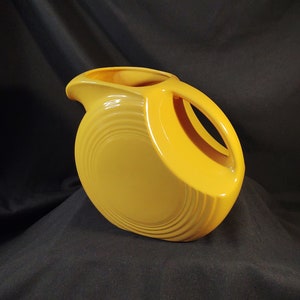 May include: A yellow ceramic pitcher with a unique, wavy design. The pitcher has a wide base and a narrow spout.