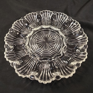 May include: A clear glass serving dish with a scalloped edge and six individual compartments. The dish has a textured, fluted design.