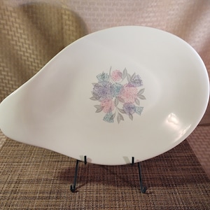 May include: White oval serving platter with a floral design in shades of pink, blue, and gray. The platter is on a black metal stand.