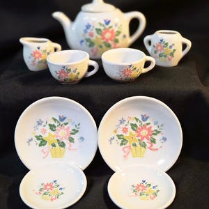 Peut inclure: Un service à thé en céramique comprenant une théière, un pot à lait, un sucrier, deux tasses, deux soucoupes et deux petites assiettes. Chaque pièce est blanche avec un motif de panier fleuri rose, jaune, bleu et vert. Couvercle inclus.