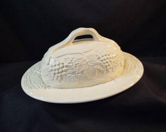 May include: White ceramic butter dish with a grapevine design. The dish has a lid with a handle and a matching base.