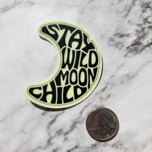 Pu&ograve; includere: Un adesivo che brilla al buio a forma di luna crescente. La luna &egrave; riempita con il testo "Stay Wild Moon Child" in nero.