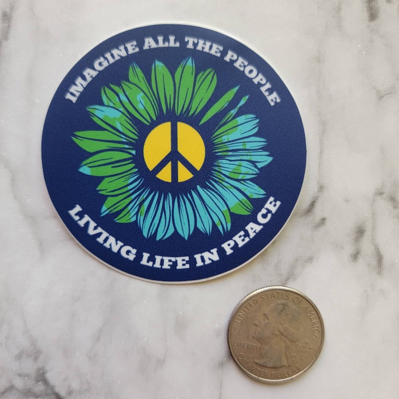 May include: A blue and green round sticker with a peace sign and a flower design. The text "Imagine All The People Living Life In Peace" is written around the edge of the sticker.