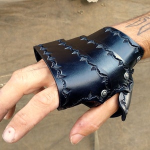 A leather demi gauntlet, shown being worn from the viewer's POV. It is dyed black with a tooled border.