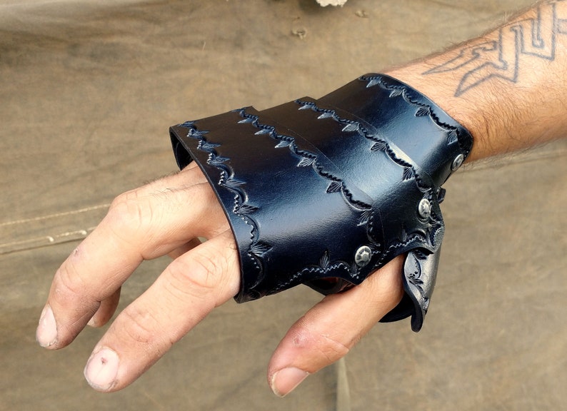 A leather demi gauntlet, shown being worn from the viewer's POV. It is dyed black with a tooled border.