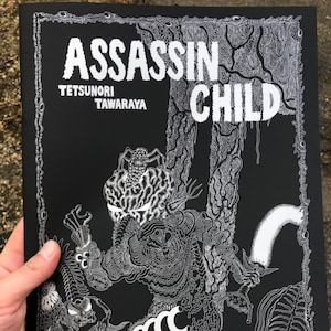 May include: Black and white illustration of a comic book cover with the title "Assassin Child" by "Tetsunori Tawaraya". The cover features a detailed drawing of a monstrous creature with a spider on its head.