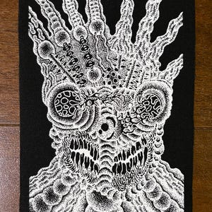 Könnte beinhalten: Schwarz-weißer Aufnäher mit einer detaillierten, abstrakten Illustration einer Kreatur mit großen Augen und einem strukturierten, organischen Design. Das Kunstwerk weist einen hohen Detailgrad mit komplizierten Mustern und Schattierungen auf. Der Aufnäher ist rechteckig.