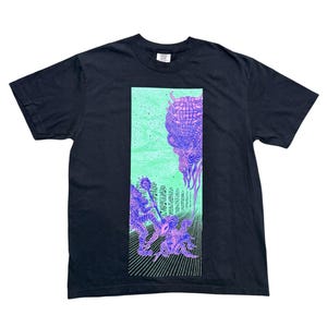Puede incluir: Una camiseta negra de manga corta con un estampado gráfico rectangular en el pecho. El diseño muestra un fondo verde claro con ilustraciones de líneas moradas de dos figuras en conflicto y una criatura grande en la parte superior.