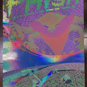 May include: A holographic concert poster for Phish at Fenway Park, Boston, MA, July 31 and August 1, 2026. The artwork features a large, spiky, orange-toned creature looming over a baseball stadium with small skeletal figures playing on the field.
