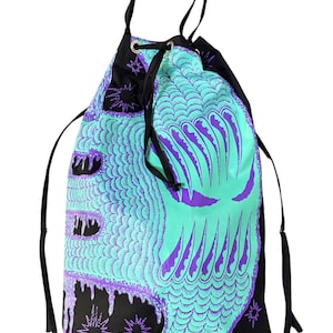 May include: A drawstring backpack with a teal and purple monster face design. The bag features a black top and straps, with a repeating scale pattern and starburst accents. The monster face has large, jagged teeth.
