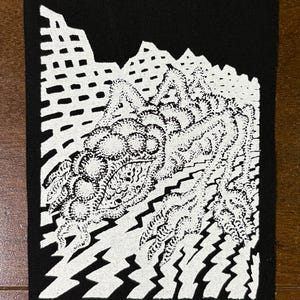 Könnte beinhalten: Schwarzer rechteckiger Aufnäher mit weißem Grafikdesign. Das Design zeigt eine Bergkette, eine detaillierte zentrale organische Form und gezackte blitzartige Formen. Wahrscheinlich für Kleidung oder Accessoires.