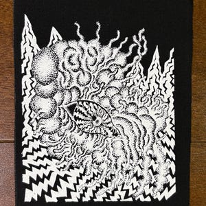 Könnte beinhalten: Schwarzer Aufnäher mit einem weißen, abstrakten Design. Das Design zeigt eine zentrale augenartige Form, die von wirbelnden, gepunkteten Mustern und gezackten, bergähnlichen Kanten umgeben ist. Das Kunstwerk ist ein starker Kontrast von Schwarz und Weiß.