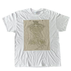 May include: A white short-sleeve t-shirt featuring a large rectangular beige patch on the chest. The patch displays a detailed line art illustration of a small animal resting inside a large mushroom, with flowing root-like structures below.