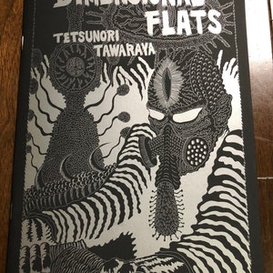 May include: A black and silver comic book cover with the title "DIMENSIONAL FLATS" and the author's name "TETSUNORI TAWARAYA". The cover features a detailed illustration of a creature with a gas mask and a third eye.
