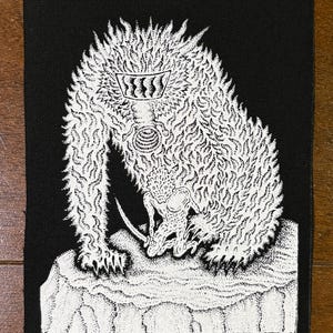 Könnte beinhalten: Schwarzer Aufnäher mit einer detaillierten weißen Illustration einer Kreatur mit Krone und Schwert. Die Kreatur hat einen pelzigen Körper und steht auf einer gepunkteten Felsformation. Das Kunstwerk ist vor schwarzem Hintergrund.
