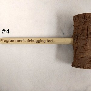 Pode incluir: Um martelo de madeira com acabamento em casca natural e uma al&ccedil;a que diz "Ferramenta de depura&ccedil;&atilde;o para programadores."