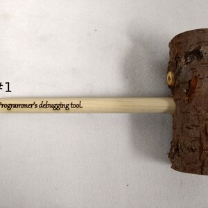 Pode incluir: Um martelo de madeira com acabamento de casca natural e um cabo de madeira. O cabo &eacute; gravado com o texto "Ferramenta de depura&ccedil;&atilde;o para programadores."