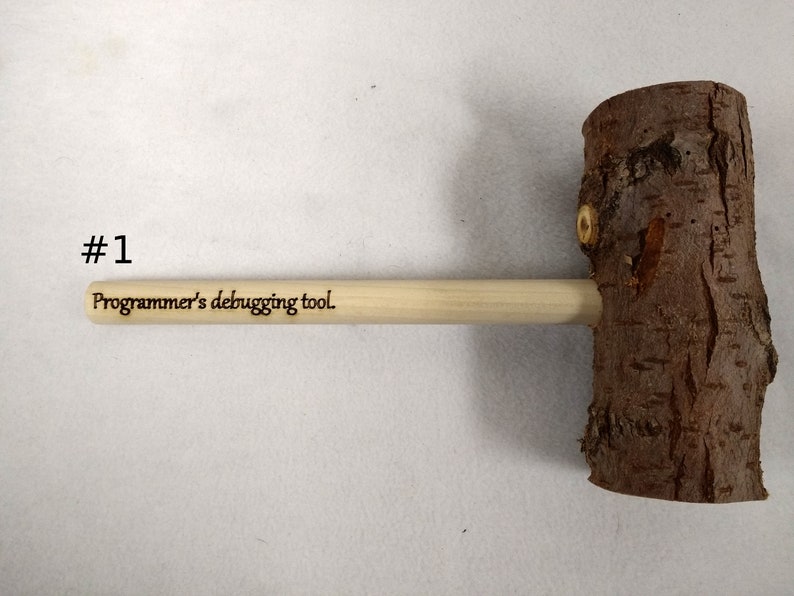Pode incluir: Um martelo de madeira com acabamento de casca natural e um cabo de madeira. O cabo &eacute; gravado com o texto "Ferramenta de depura&ccedil;&atilde;o para programadores."