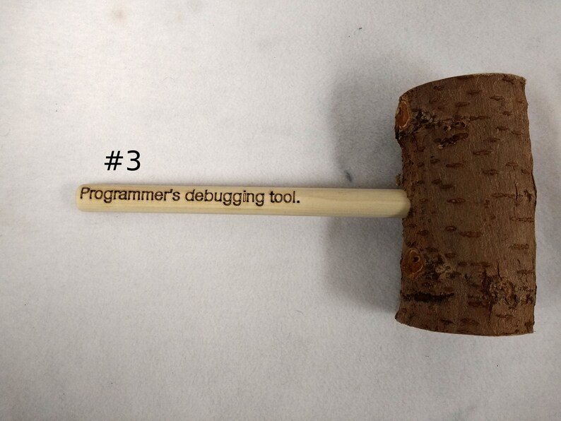 Pode incluir: Um martelo de madeira com uma al&ccedil;a que diz "Ferramenta de depura&ccedil;&atilde;o para programadores". O martelo &eacute; feito de madeira natural com uma textura de casca &aacute;spera.