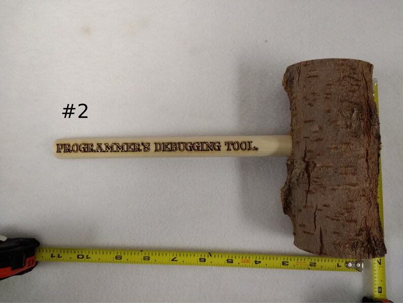Pode incluir: Um martelo de madeira com acabamento em casca natural e uma al&ccedil;a que diz "PROGRAMMER'S DEBUGGING TOOL."