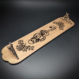 May include: Wooden wand holder with a black snake and skull design, a dark triangle symbol, and floral accents.