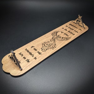 May include: Wooden bookmark with a phoenix design and the quote "Happiness can be found even in the darkest of times if one only remembers to turn on the light." The bookmark also features a symbol of the Deathly Hallows.