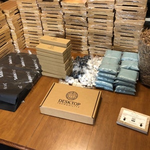 May include: A brown cardboard box with the text "Desktop Tranquility" printed on the top. The box is surrounded by various items, including small bags of sand, white and black stones, and a stack of brown cardboard boxes.