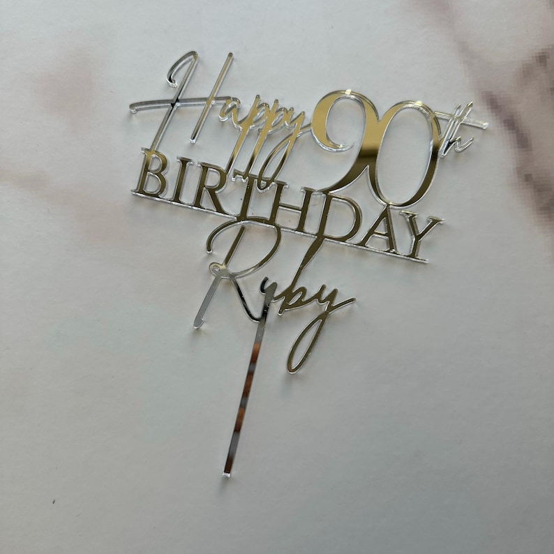 May include: Silver mirror acrylic cake topper with the text "Happy 90th Birthday Ruby".