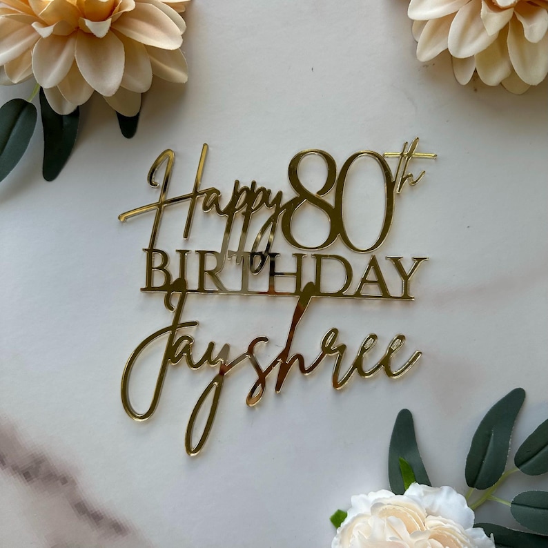 May include: Gold acrylic cake topper with the text "Happy 80th Birthday Jayshree".