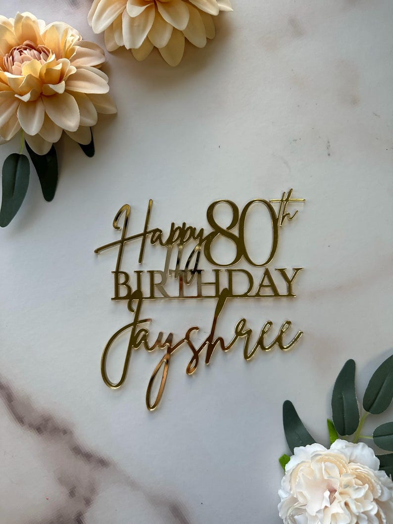 May include: Gold glitter cake topper with the text "Happy 80th Birthday Jayshree".