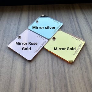 May include: Three square pieces of acrylic mirror glass in rose gold, silver, and gold. Each piece has the text "TroGlass Mirror" and the color of the mirror printed on it.