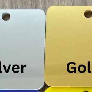 May include: Two square metal tags with rounded corners and a hole in the center. The tag on the left is silver and says "Silver". The tag on the right is gold and says "Gold".