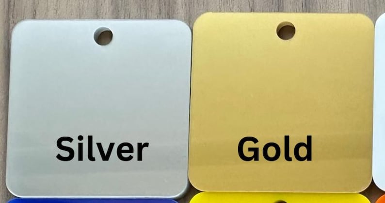 May include: Two square metal tags with rounded corners and a hole in the center. The tag on the left is silver and says "Silver". The tag on the right is gold and says "Gold".