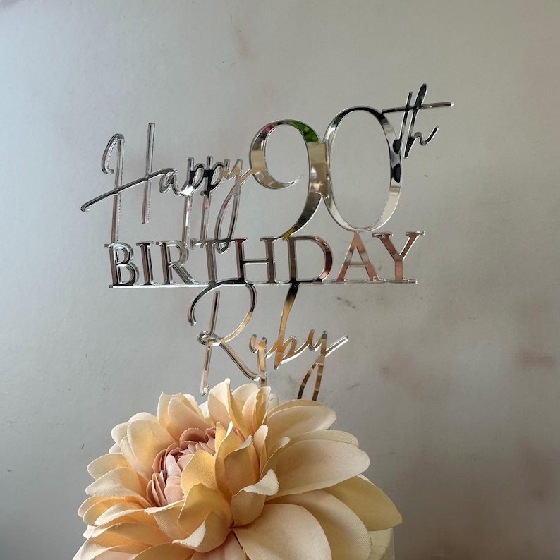 May include: Silver mirror acrylic cake topper with the text "Happy 90th Birthday Ruby".