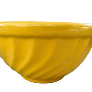 May include: A bright yellow ceramic mixing bowl with a glossy finish and a distinct spiral fluted pattern along the exterior sides. The bowl features a wide, rounded rim and a tapered base, showcasing a smooth, uniform color throughout the piece.
