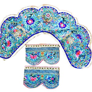 May include: An ornate, embroidered headpiece and two matching panels. The headpiece is a scalloped shape, with a blue and turquoise background, and floral and bird embroidery. The panels have a similar design. The trim is gold and white.