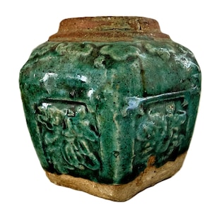 May include: A square-shaped ceramic jar with a vibrant green crackle glaze finish. The vessel features raised relief patterns on each side and a wide, unglazed brown rim at the top. The base is also unglazed, showing a light tan, textured material.