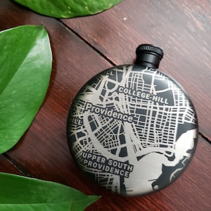 Könnte beinhalten: Eine schwarze Metallflasche mit einer silbernen Karte von Providence, Rhode Island, die auf der Vorderseite graviert ist. Die Karte enthält die Namen von Stadtteilen wie College Hill und Upper South Providence.