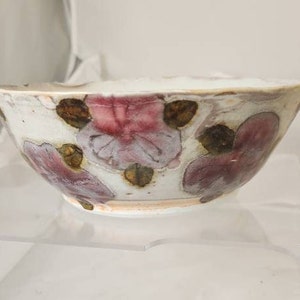 May include: A white ceramic bowl with a floral design. The bowl features pink and brown flower patterns against a white background. The bowl is on a clear surface.