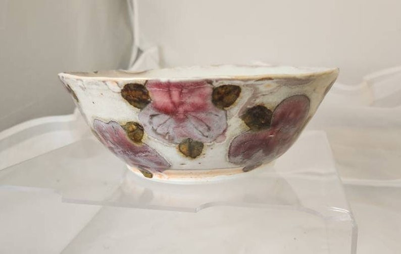 May include: A white ceramic bowl with a floral design. The bowl features pink and brown flower patterns against a white background. The bowl is on a clear surface.