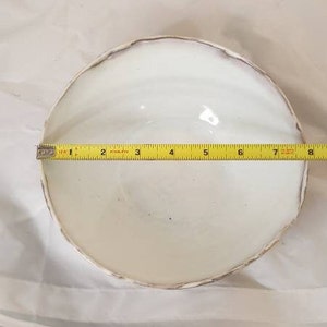 May include: A white ceramic bowl with a textured rim, approximately 20 cm in diameter, is measured with a yellow tape measure. The bowl is set against a white background.