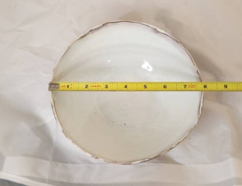 May include: A white ceramic bowl with a textured rim, approximately 20 cm in diameter, is measured with a yellow tape measure. The bowl is set against a white background.