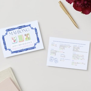May include: Two white cards with text and illustrations on a light background. One card features "MAHJONG" in blue, with illustrations of tiles and "2025 CARD SEQUENCE". The other card has text and illustrations. A gold pen and a red flower are also present.