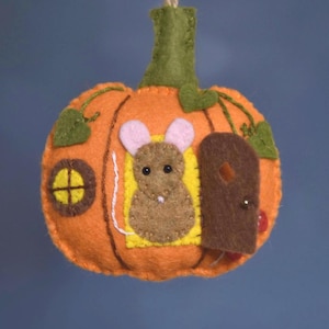 Peut inclure: Ornement de citrouille en feutre orange fait à la main, avec une tige et des feuilles vertes. La citrouille représente une maison en forme de souris avec une porte marron, une fenêtre jaune et une souris marron aux oreilles roses. Une ficelle est attachée pour suspendre.