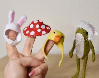 May include: A set of three felt finger puppets including a white rabbit ear headpiece, a red mushroom cap with white spots, and a yellow duck headpiece, alongside a green felt frog figurine wearing a white fuzzy hat with pink ears.
